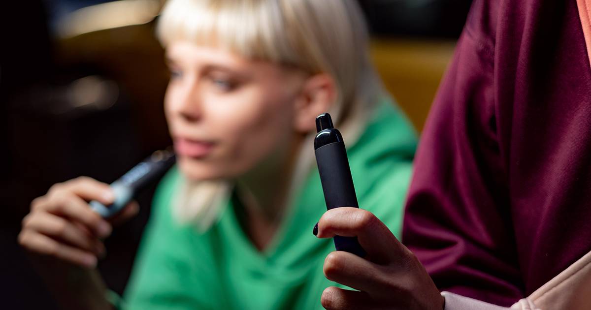 Two young adults each holding a vape