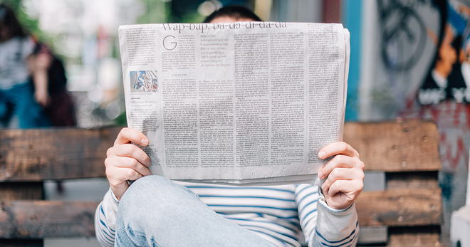 Guy reading a newspaper on a bench